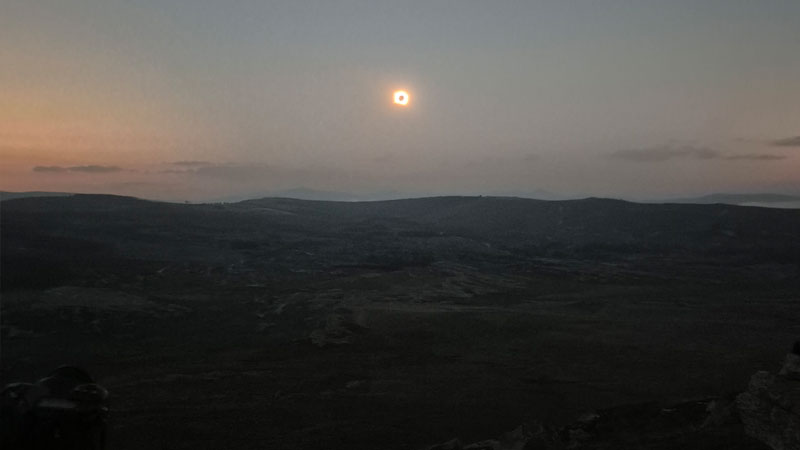 Die ringförmige Sonnenfinsternis leuchtet als schmaler heller Ring am Abendhimmel über einer dunklen Berglandschaft in Nordspanien.