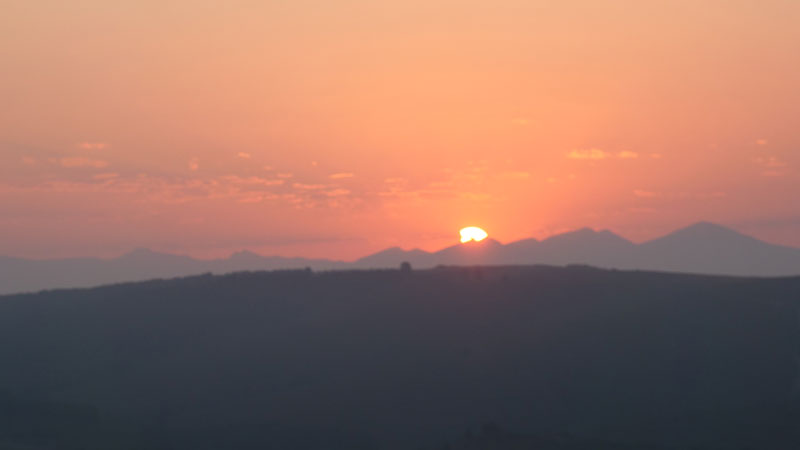 Die teilweise verfinsterte Sonne steht tief über einer dunklen Bergsilhouette und taucht den Himmel in orangefarbenes Abendlicht.